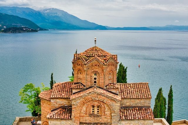Photo of a monastery in front of a lake and mountains